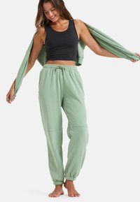 Grønne bomuldsjoggers med elastisk talje og manchetter. Parret med en sort tanktop og en matchende åben sweatshirt.