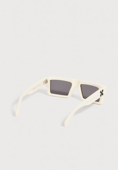 Lunettes de soleil rectangulaires blanches avec des verres foncés et un logo noir sur la branche droite, présentées sur un fond clair uni.