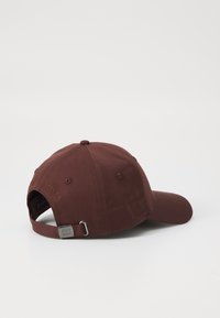 Maroon baseball cap with a curved brim, fabric texture, adjustable strap at the back, and logo detail in gold embroidery.