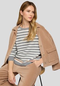 Hellbraune Cordjacke mit oversized Passform und Fronttaschen, kombiniert mit einem grau-weißen gestreiften Pullover und passenden Hosen.