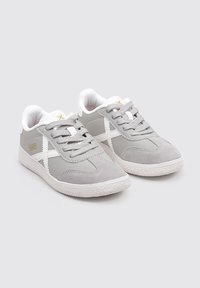 Zapatillas deportivas grises con parte superior de ante y sintético, cordones blancos y suela de goma. Presenta detalles en blanco y un logo en el costado.