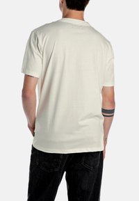 Lys beige t-shirt med korte ærmer, rund udskæring og en glat tekstur. Bagsiden viser minimale syninger og en afslappet pasform.
