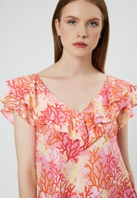 Roze jurk met koraalpatroon, voorzien van ruches op de korte mouwen en een V-hals. De stof is lichtgewicht met een soepele textuur.