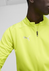 Helle gelbe Sport-Zip-Jacke aus strukturiertem Stoff, ausgestattet mit einem Stehkragen und einem weißen Puma-Logo auf der linken Brust.