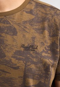 Bruine T-shirt met korte mouwen, featuring een gestructureerd houtpatroon en donkerbruine accenten. Inclusief geborduurd logo in de linkeronderhoek.