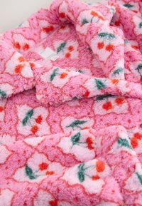 Weicher rosa Fleecefaserstoff mit roten und grünen Blumenmustern, ausgestattet mit einem Kragen und einem sichtbaren Kleidungslabel innen.