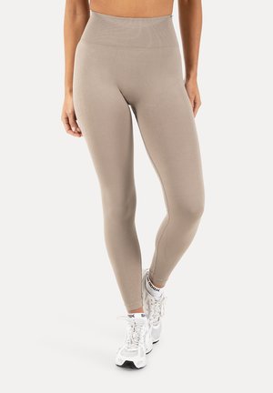 Beżowe legginsy z wysokim stanem i obcisłym krojem, noszone z białymi skarpetkami do kostek i białymi butami do biegania, pokazane od talii do stóp.