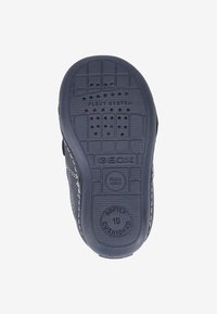 Semelle de chaussure en caoutchouc noir avec surface texturée, présentant des empreintes "FLEXY SYSTEM" et "GEOX". Comprend des trous de drainage et des détails de rembourrage.