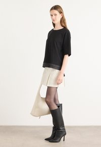 Black short-sleeve top with a sheer hem, paired with a beige pleated skirt. Black knee-high stiletto boots and a cream shoulder bag.