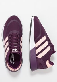 Lila sportskor med rosa ränder och detaljer, utrustade med ett texturerat tygöverdrag, snörningsdesign och en dämpad sula.