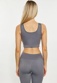 Crop top sportivo grigio con scollatura arrotondata e spalline larghe, abbinato a leggings a vita alta coordinati. Il materiale appare liscio con una leggera lucentezza.