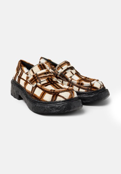 Een paar chunky zwarte loafers met een bruin en witte geblokte bontpatroon en moc-toe stiksel op een witte achtergrond.