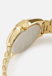 Goldfarbene Uhr mit rundem Gehäuse, ausgestattet mit einer polierten Lünette, einer strukturierten Krone und einem Metallarmband. Glatter Rücken mit einem Logo-Prägung.