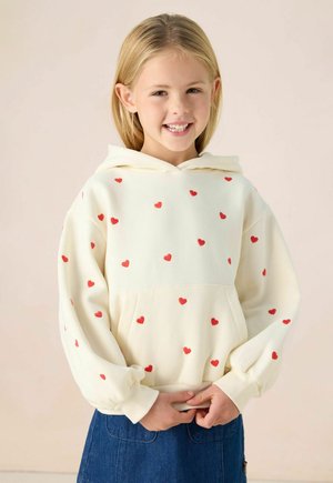 Un sweat à capuche crème avec des motifs de cœurs rouges, des manches longues, une capuche avec cordon de serrage et une poche kangourou, associé à une jupe en denim.