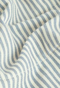 Geweven stof met afwisselend blauwe en witte strepen, met een zachte textuur en een subtiel diagonaal patroon. Toont stiksel details.