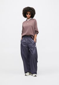 Καφέ φούτερ με λευκό γιακά, συνδυασμένο με σκούρο μπλε, φαρδιά παντελόνια και λευκά αθλητικά παπούτσια. Το σύνολο ολοκληρώνεται με ανοιχτόχρωμα γυαλιά ηλίου.