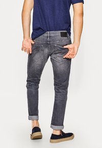 Jeans de mezclilla gris con corte ajustado, que cuentan con bolsillos traseros y una etiqueta de cuero. Con puños enrollados y combinados con zapatos de ante azul marino.