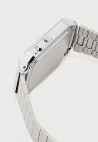 Sølv metal ur med rektangulært urskive, to sideknapper og et kædearmbånd design. Glat, poleret finish med en refleksiv overflade.