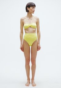 Gelbes Bikini-Set mit einem bandeauartigen Oberteil mit Knoten und einem hochgeschnittenen Unterteil. Hergestellt aus glattem Material mit einer körperbetonten Passform.