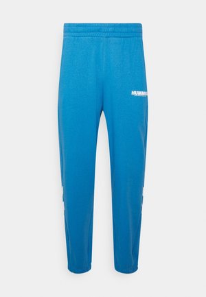 Niebieskie spodnie sportowe z elastycznym pasem i ściągaczami, z białym logo "HUMMEL" na górnej części uda.