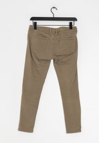 Beige stretch denim broek hangt aan een zwarte hanger. Kenmerken zijn onder andere achterzakken met een eenvoudig stiksels patroon en een slim fit ontwerp.