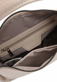 Bežinės odinės rankinės vidus su užtrauktuku, lygus tekstūra ir subtiliu siuvimu; juodi užtrauktuko dantukai sustiprina kontrastą.