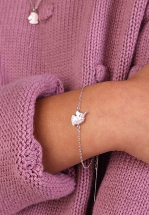 Zilveren schakelarmband met een kleine eenhoorncharme met roze accenten, gedragen over een lichtpaarse gebreide trui. De textuur is zacht en comfortabel.