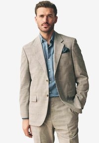 Traje a cuadros gris claro con un corte ajustado y dos botones, combinado con una camisa de mezclilla azul y un pañuelo negro en el bolsillo.