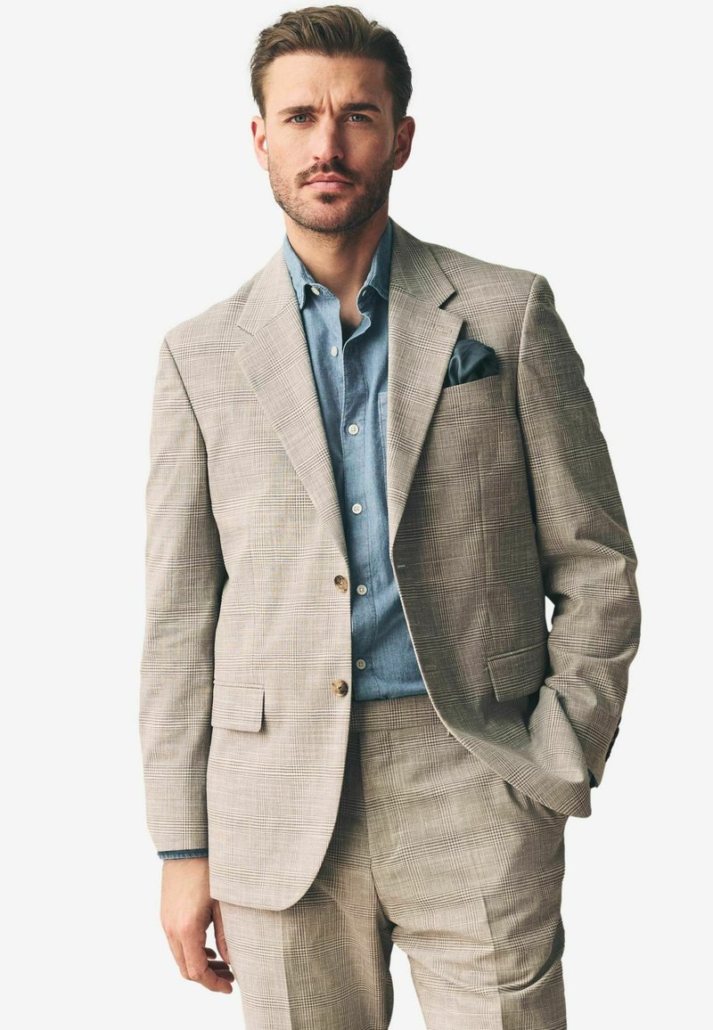 Traje a cuadros gris claro con un corte ajustado y dos botones, combinado con una camisa de mezclilla azul y un pañuelo negro en el bolsillo.