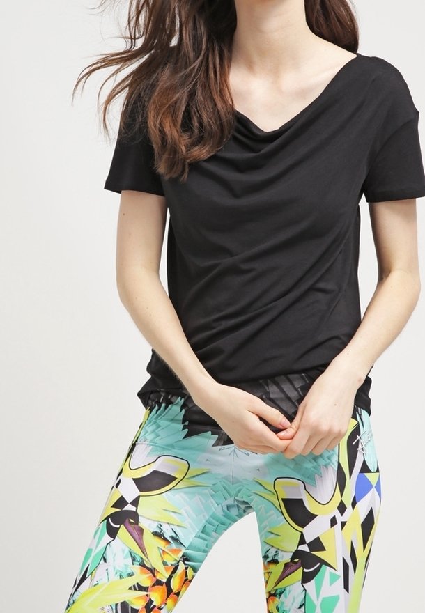 Top corto a maniche corte nero con drappeggio abbinato a leggings multicolori con motivi tropicali e forme geometriche.