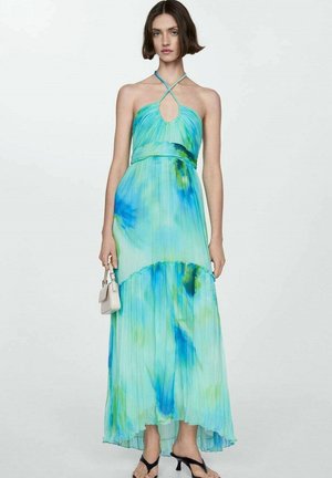 Maxi haljina, plisirani materijal u aqua i zelenom tie-dye uzorku, halterneck izrez s dekolteom, lepršavi siluet, u kombinaciji s crnim sandalama.