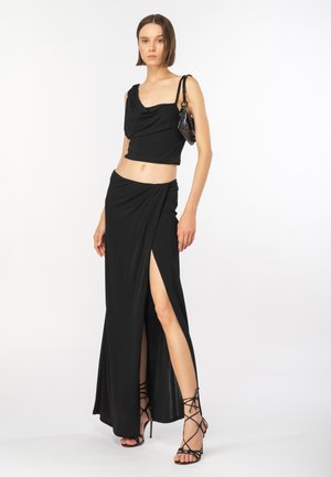 Completo black a due pezzi con top drappeggiato e gonna lunga fino al pavimento con una spacco alto fino alla coscia. Tessuto liscio e aderente con dettagli minimi.