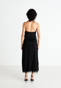 Black strapless dress featuring a textured fringe design, knee-length, with a fitted bodice and flowing skirt. Worn with high-heeled sandals.