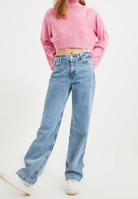 Lichtblauwe denim jeans met wijde pijpen en een hoge taille. Gecombineerd met een cropped, roze ribgebreide coltrui. Witte sneakers maken de outfit compleet.