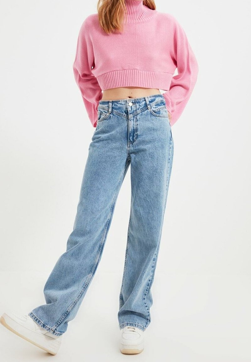 Lichtblauwe denim jeans met wijde pijpen en een hoge taille. Gecombineerd met een cropped, roze ribgebreide coltrui. Witte sneakers maken de outfit compleet.