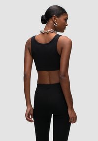 Zwarte cropped tanktop met geribbeld textuur, gecombineerd met hoge zwarte legging. Model toont de achterkant, met een minimalistische zilveren ketting.