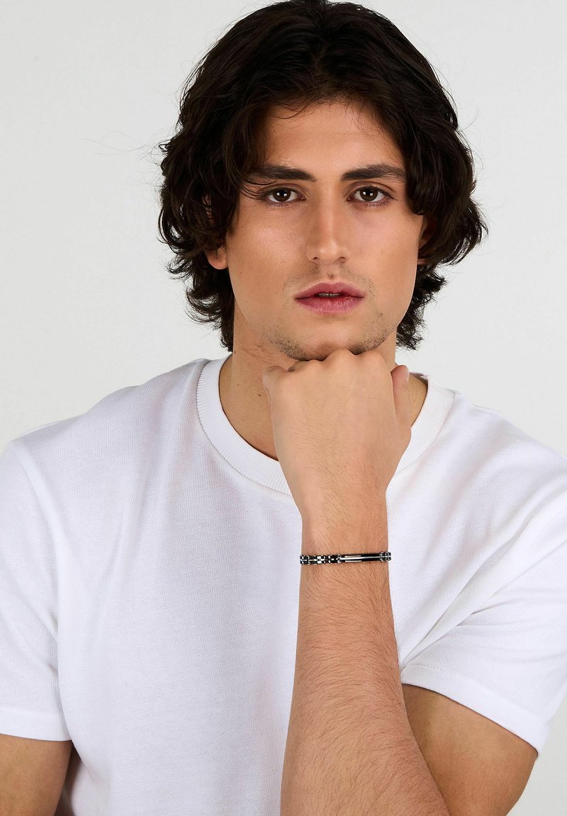 Bracciale tono argento con perline cilindriche e rettangolari, caratterizzato da un design flessibile e dettagli testurizzati, indossato su un polso nudo.