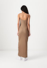 Brązowa maks sundress z żebrowym wzorem i wycięciem na plecach, z bocznymi rozcięciami i cienkimi ramiączkami. Noszona z białymi sneakersami w casualowym stylu.