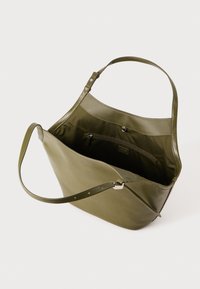 Sac fourre-tout en cuir vert olive avec une texture lisse, une longue sangle réglable et une poche zippée intérieure. Ouverture sur le dessus avec une forme douce et non structurée.