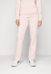 Sweatshirt atlético rosa claro com um bolso frontal e calças de jogger combinantes. Ambos são feitos de um tecido macio com um ajuste descontraído. Ténis brancos destacam o visual.