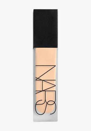Bouteille rectangulaire en verre dépoli avec bouchon noir, remplie de liquide beige clair. Grand logo NARS noir imprimé verticalement sur le devant.
