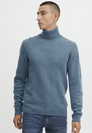 Blue turtleneck sweater made of soft fabric, featuring a ribbed neck and cuffs, and a standard fit, paired with dark jeans.