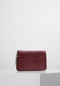 Burgundská koženka taška přes rameno s krokodýlí texturou, zlatým řetízkovým popruhem a obdélníkovým tvarem, s hladkým povrchem.