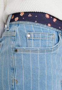 Jeans de mezclilla de rayas azul claro con una cinturilla de patrón floral en color navy y acentos de metal en los bolsillos. Tejido texturizado, diseño casual.