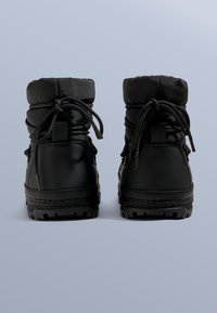 Černé nepromokavé zimní boty s polstrovaným vrškem, nastavitelnými tkaničkami a odolnou gumovou podrážkou s texturovaným protiskluzovým vzorem.