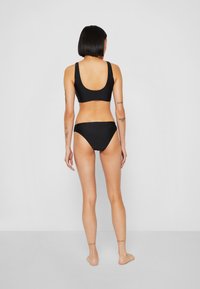 Set bikini nera composto da un top a scollo rotondo e un capo inferiore a vita bassa, entrambi in tessuto liscio. Il design offre una silhouette minimalista.