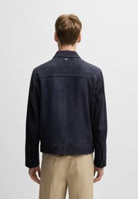 Navy suede jacket with a pointed collar, long sleeves, buttoned cuffs, and a simple logo at the back. Features a tailored fit and clean lines.