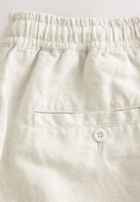 Light gray elastic-waist shorts made from textured fabric. Features a single back pocket with a white button and subtle stitching details.