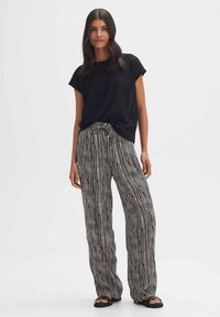 Zwarte gebreide top met korte mouwen en een losse fit, gecombineerd met gestreepte wijde broek in zwart en wit. Slippers maken de outfit compleet.