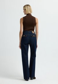 Top sin mangas marrón de canalé combinado con unos jeans de pierna ancha de tiro alto en azul oscuro, que cuentan con dos bolsillos traseros y detalles en oro.